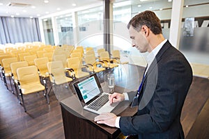 Concentrated speaker standing at tribune and using laptop