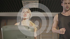Concentrated sport couple talking in gym. Closeup couple running on treadmill