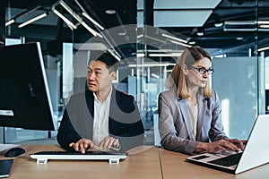 Team of business partners working together on computer and laptop, Asian man and woman in a modern office