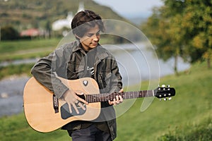 Concentrated teenage boy musician playing acoustic guitar outdoor. Handsome boy love misuc