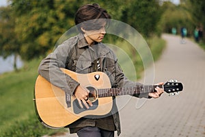 Concentrated teenage boy musician playing acoustic guitar outdoor. Handsome boy love misuc