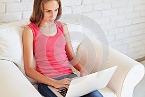 Concentrated teenage girl typing something on her laptop at home