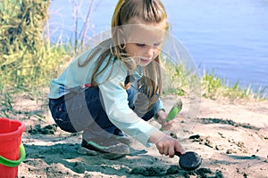 Concentrated toddler playing with his toy bucket and shovel near the river. Springtime and early morning. Investigate  details of