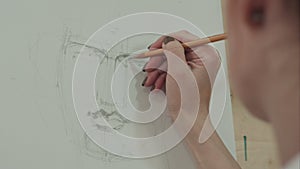 Concentrated woman artist painting classical man portrait with pencil