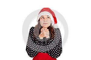 Concentrated woman in dress praying with pray gesture and looking up. emotional girl in santa claus christmas hat isolated on whit