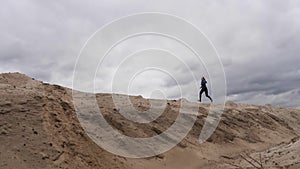Concentrated woman jogger with a slender figure is engaged in run at desert. Dark storm clouds sky at background.