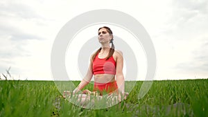 Concentrated woman in lotus pose doing meditation in green field. Calm yoga concept, religion, zen, peaceful mind