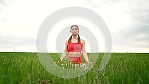 Concentrated woman in lotus pose doing meditation in green field. Calm yoga concept, religion, zen, peaceful mind
