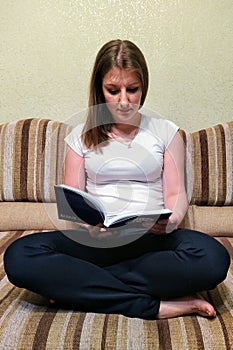 Concentrated woman sit on sofa and read book