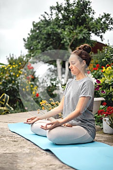 Concentrated woman sitting in lotus position yoga at summer garden park plants and blossom flowers