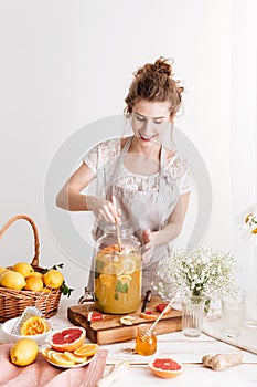 Concentrated woman standing indoors cooking citrus beverage