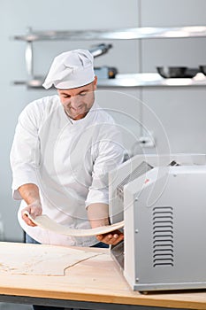 Concentrated at work. Handsome chef rolling a dough through pasta machine