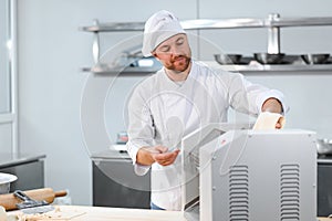 Concentrated at work. Handsome chef rolling a dough through pasta machine
