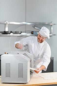 Concentrated at work. Handsome chef rolling a dough through pasta machine