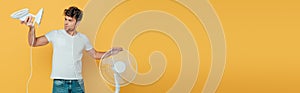 Concentrated and worried man looking at desk fan isolated on yellow