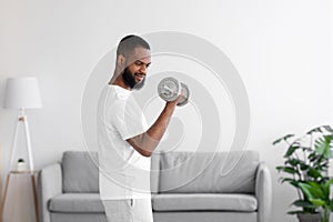 Concentrated young bearded african american man in white clothes lifting dumbbells