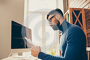 Concentrated young bearded businessman in glasses reading contract