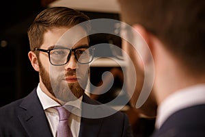 Concentrated young bearded businessman looking at mirror.