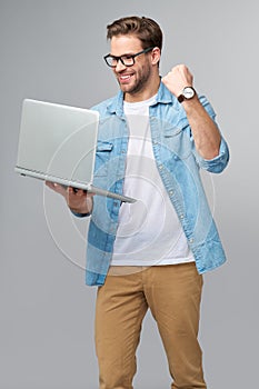 Concentrated young bearded man wearing glasses dressed in jeans shirt holding laptop isolated over grey studio