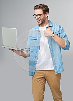 Concentrated young bearded man wearing glasses dressed in jeans shirt holding laptop isolated over grey studio