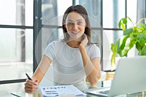 Concentrated young beautiful businesswoman working on laptop in bright modern office