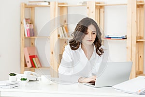 Concentrated young beautiful businesswoman working on laptop and document in bright modern office