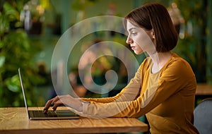 Concentrated young brunette woman developer working at cafe, using laptop