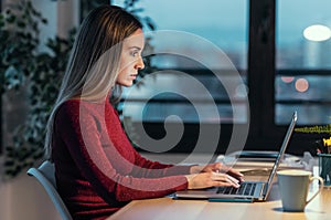 Concentrated young business woman working with laptop in the office at night