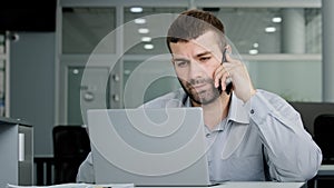 Concentrated young businessman speaks on phone consults client checks data on laptop screen serious manager remote