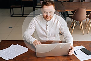 Concentrated young businessman wearing fashion casual clothing is typing on laptop computer
