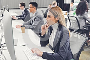 Concentrated young businesswoman using desktop computer while working with colleagues