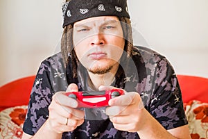 Concentrated young caucasian man with dreadlocks sitting on the couch playing video games