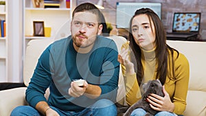 Concentrated young couple sitting on couch eating fried chicken