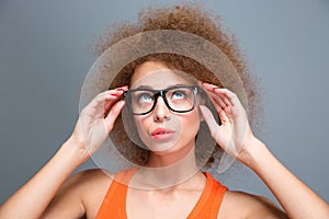 Concentrated young curly woman in black glasses looking up