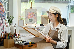 Concentrated young female artist painting picture with watercolor at cozy studio. Art, creative hobby and leisure