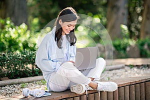 Concentrated young female sitting cross-legged on a bench in a lush garden