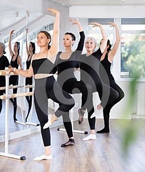 Young girl practicing in passe position at barre during group ballet class photo