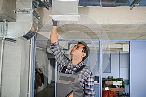 Concentrated young Indian engineer setting up air conditioner.