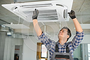 Concentrated young Indian engineer setting up air conditioner.