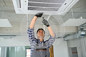 Concentrated young Indian engineer setting up air conditioner.