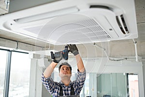 Concentrated young Indian engineer setting up air conditioner.