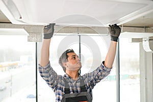 Concentrated young Indian engineer setting up air conditioner.