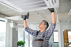 Concentrated young Indian engineer setting up air conditioner.