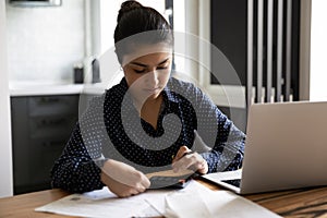 Concentrated young indian lady engaged in paperwork using computer calculator