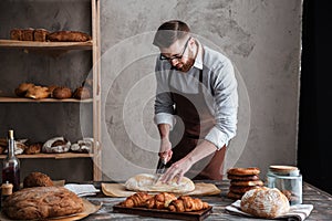 Concentrated young man baker cut the bread.