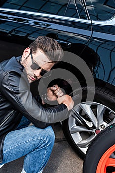 concentrated young man in sunglasses using wheel spanner for wheel replacement