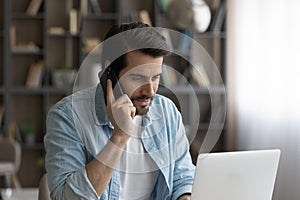 Concentrated young man talking on phone, working on computer.