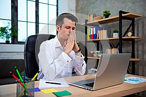 Concentrated young manager man sitting at office desk working on laptop computer and thinking about solving a financial problem