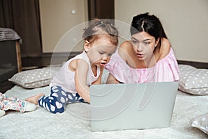 Concentrated young mother with her little daughter using laptop