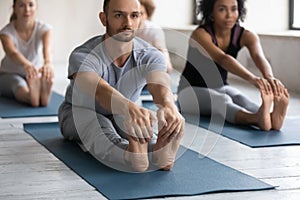 Concentrated young multiracial people practicing seated forward bend pose.